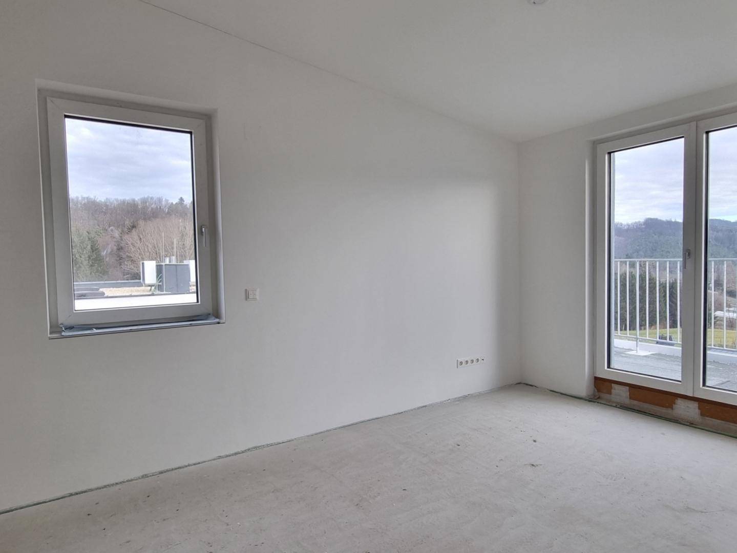 Heller Raum im Rohbau mit großem Fenster und Balkontür, die viel Licht hereinlassen.