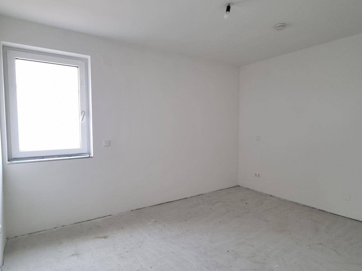 Leerer Raum im Rohbau mit einem einzelnen Fenster, bereit für den Innenausbau.