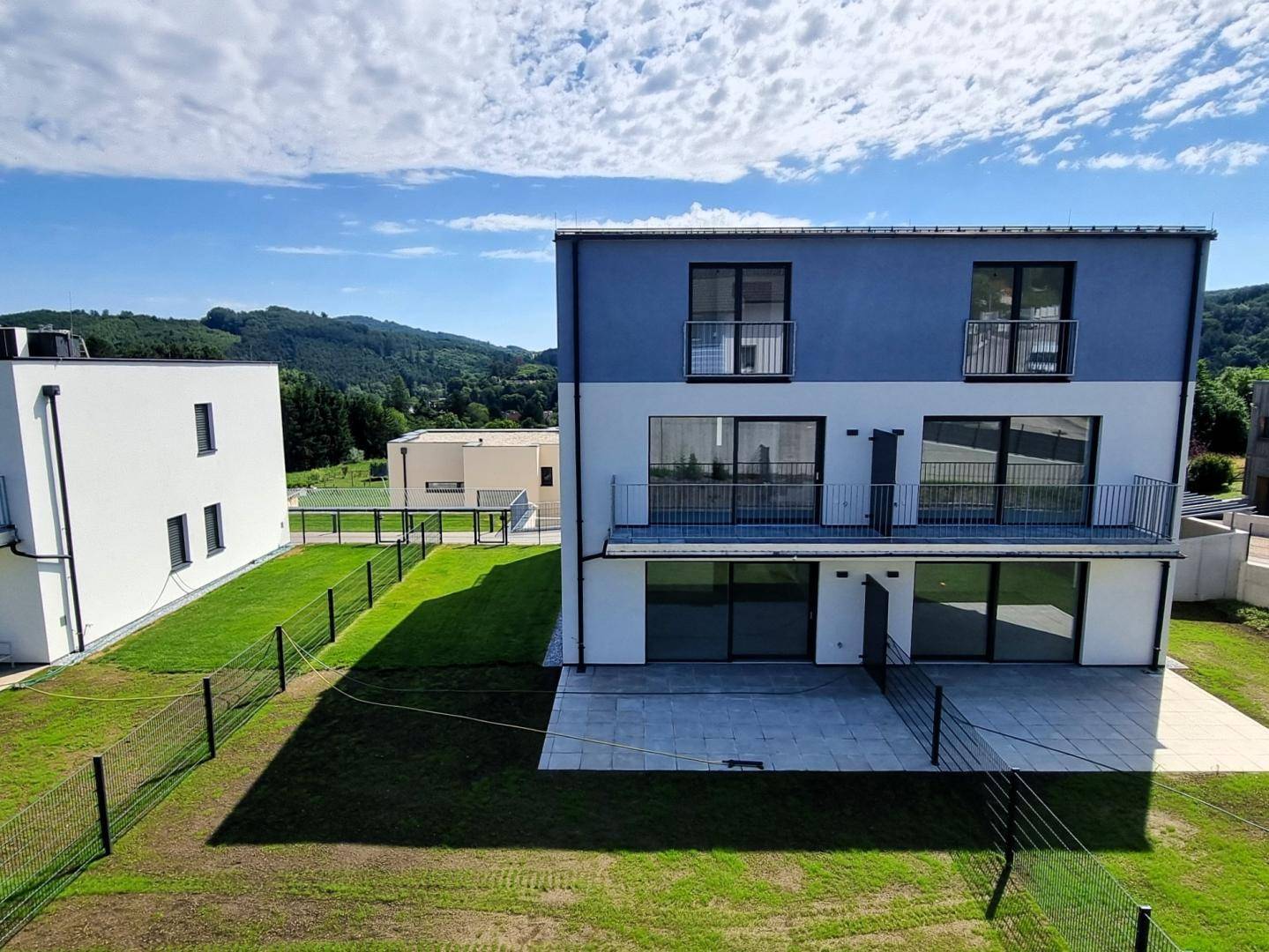 Rückansicht eines modernen Gebäudes mit Terrassenbereich, Balkonen und Blick auf die umliegende Landschaft.