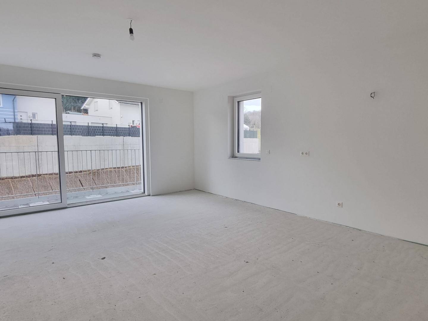 Heller, unmöblierter Wohnraum im Rohbau mit großen Schiebetüren und Blick ins Freie.