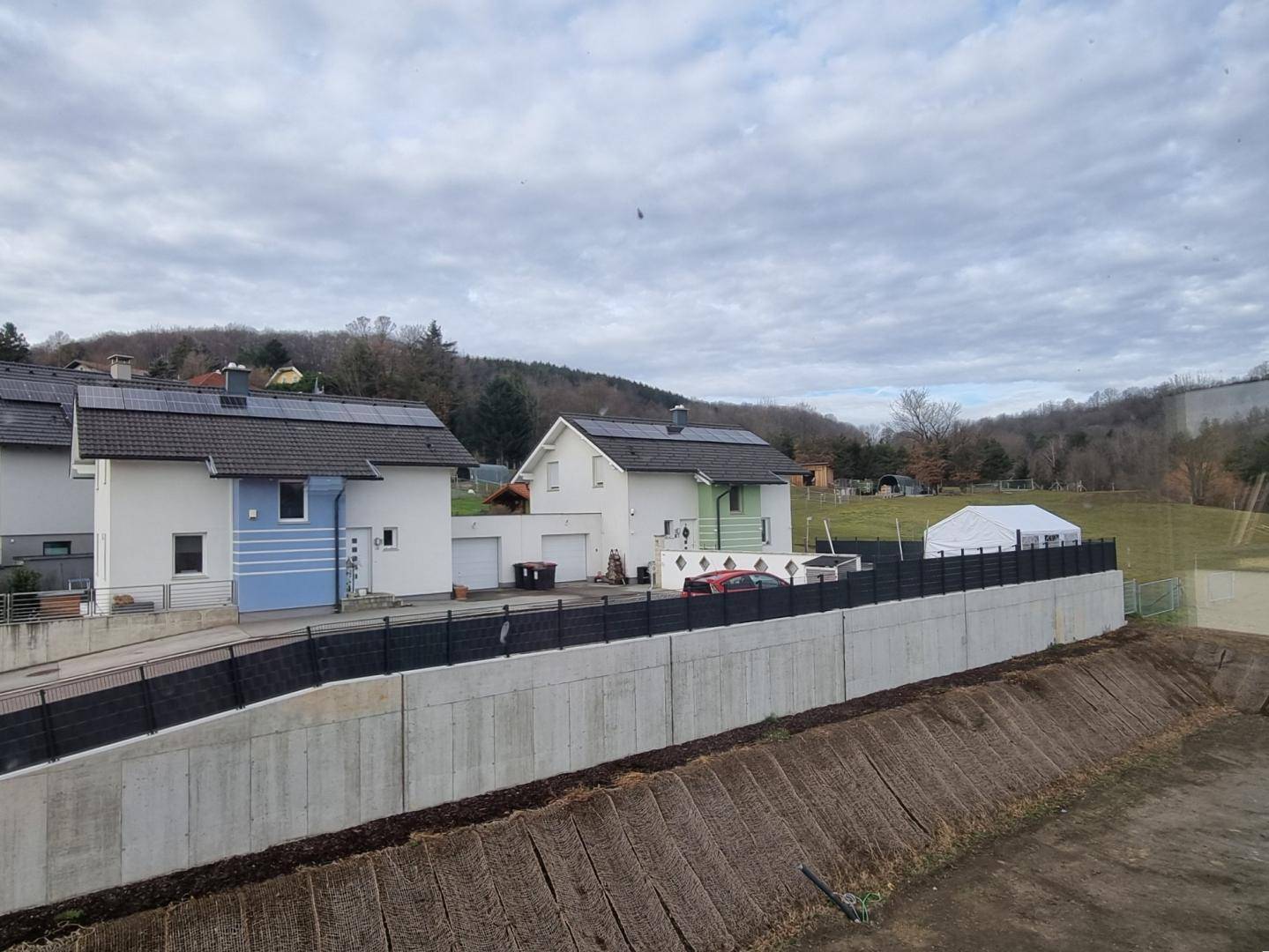 Blick auf benachbarte Häuser mit Solaranlagen und einer Betonmauer im Vordergrund.