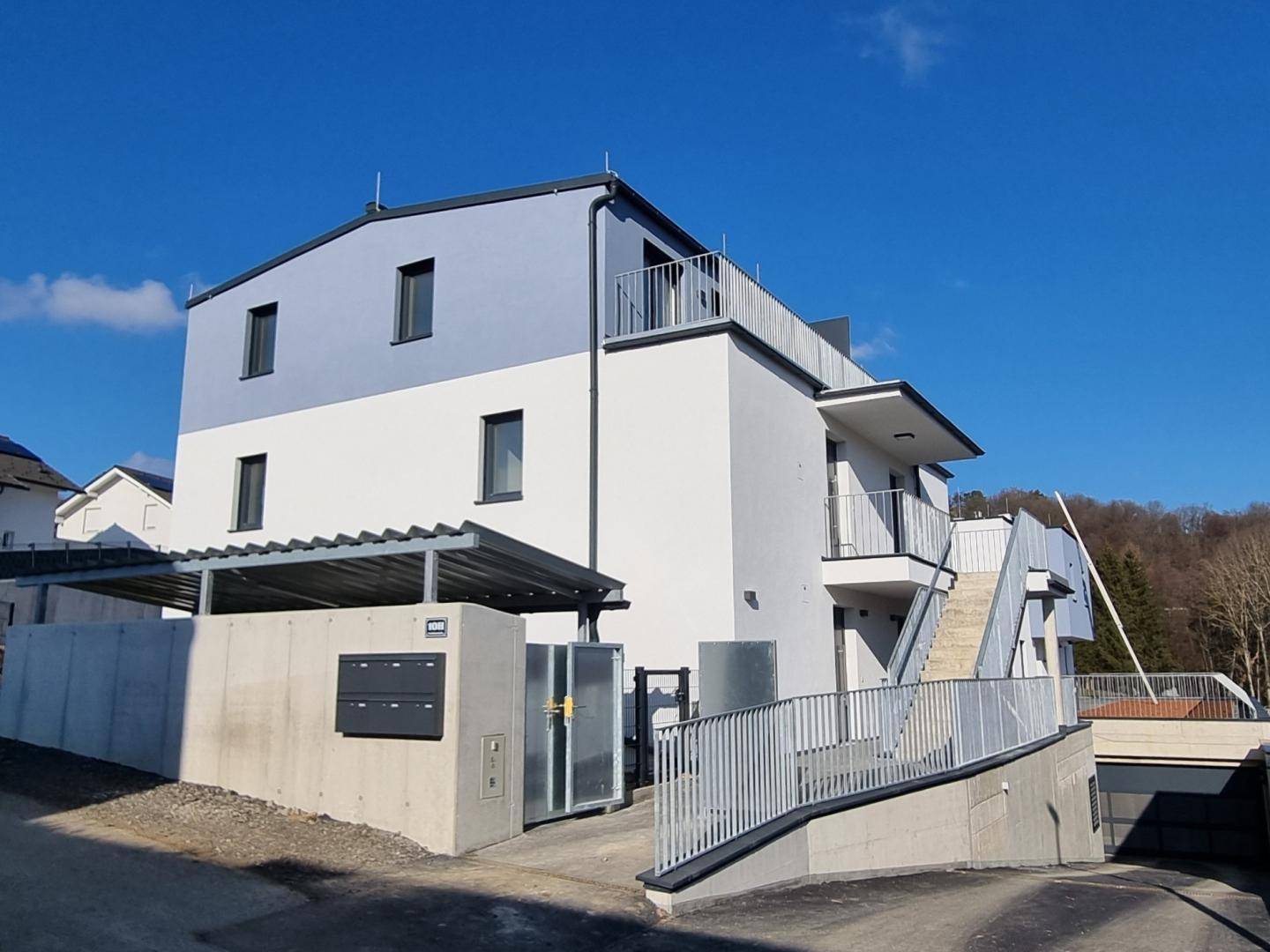 Eingangsbereich eines modernen Gebäudes mit Carport, Briefkästen und Zufahrt zur Tiefgarage.