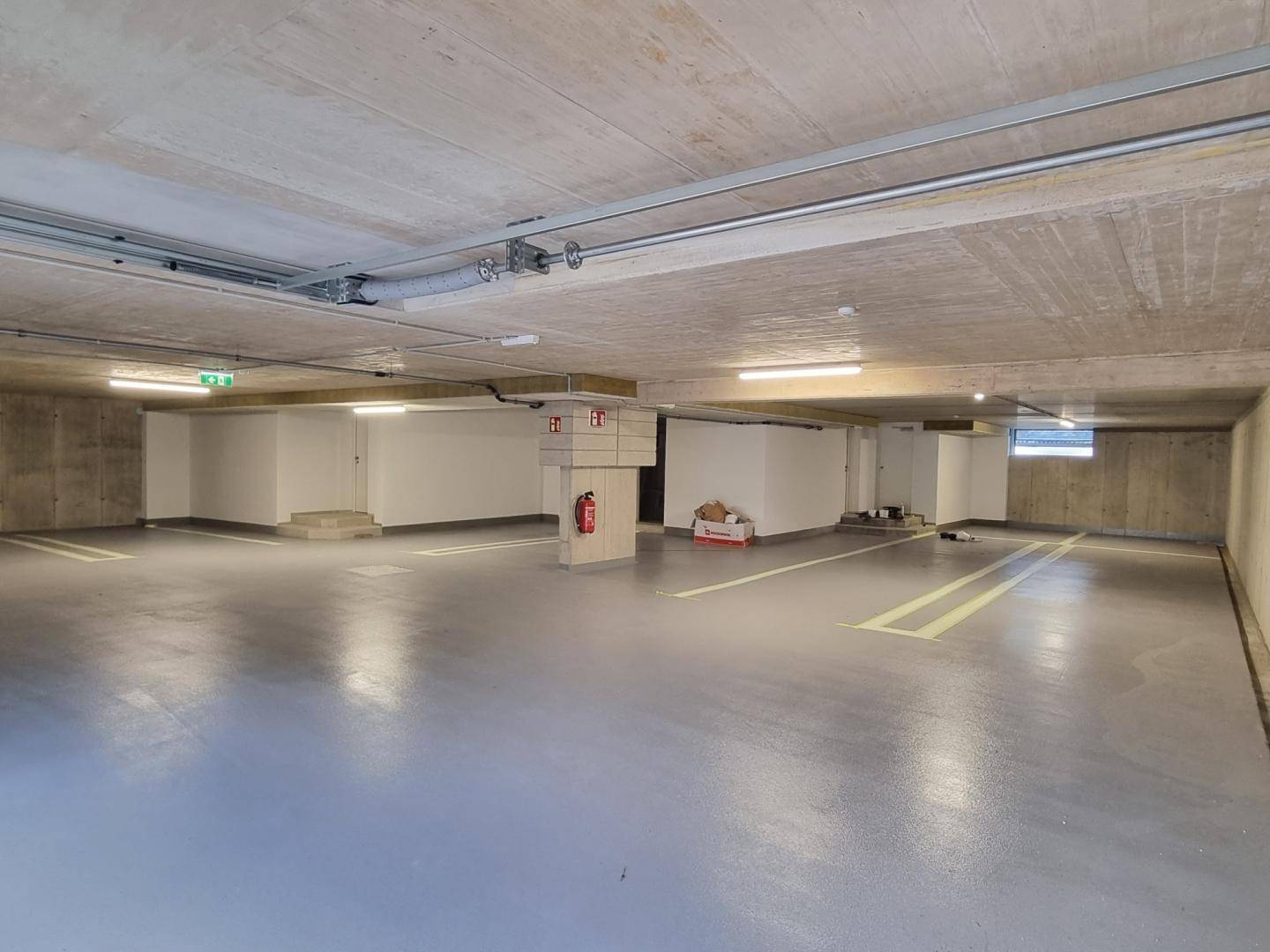 Geräumige Tiefgarage mit Betonwänden und -decken, beleuchtet und mit Parkmarkierungen versehen.