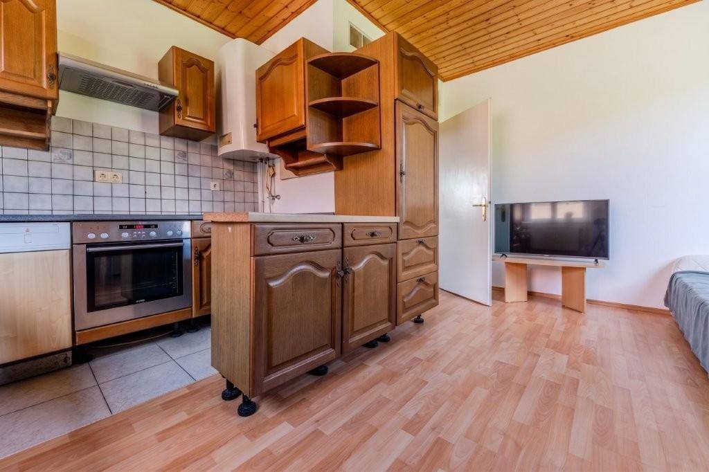 Funktionale Küche mit Holzschränken, Einbaugeräten und Fliesenboden, offen zu einem Wohn-/Schlafbereich.