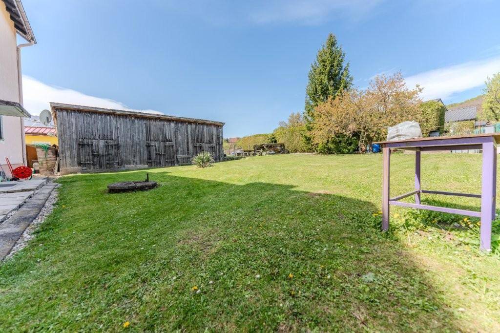 Großer, gepflegter Garten mit Rasenfläche, einem Holzschuppen und altem Baumbestand unter blauem Himmel.