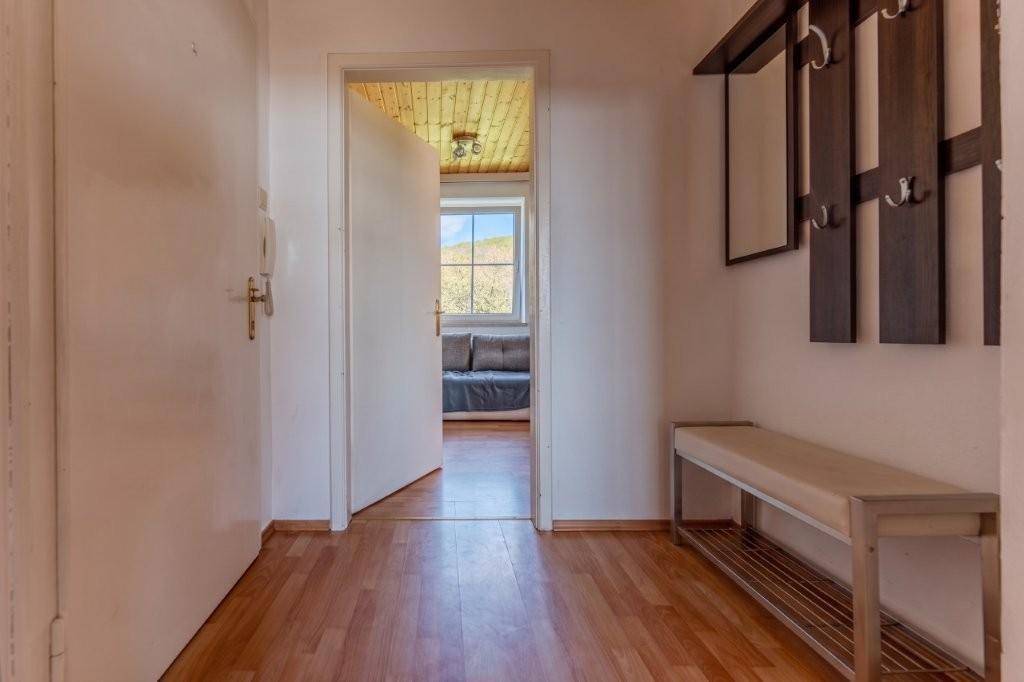 Heller Flur mit Garderobe und Sitzbank, der zu einem weiteren Zimmer mit Fenster führt.