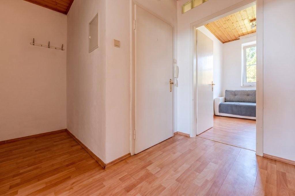 Eingangsbereich mit Garderobenhaken und hellem Laminatboden, der zu einem weiteren Wohnraum führt.