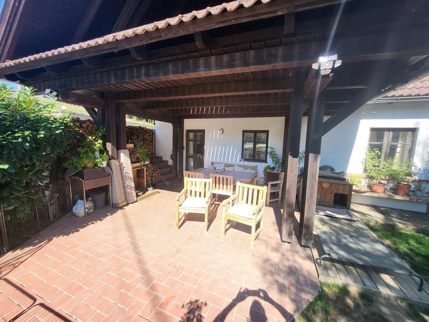 Detailansicht der überdachten Terrasse mit Holzbalken, Gartenmöbeln und einem Grillbereich für gesellige Abende.
