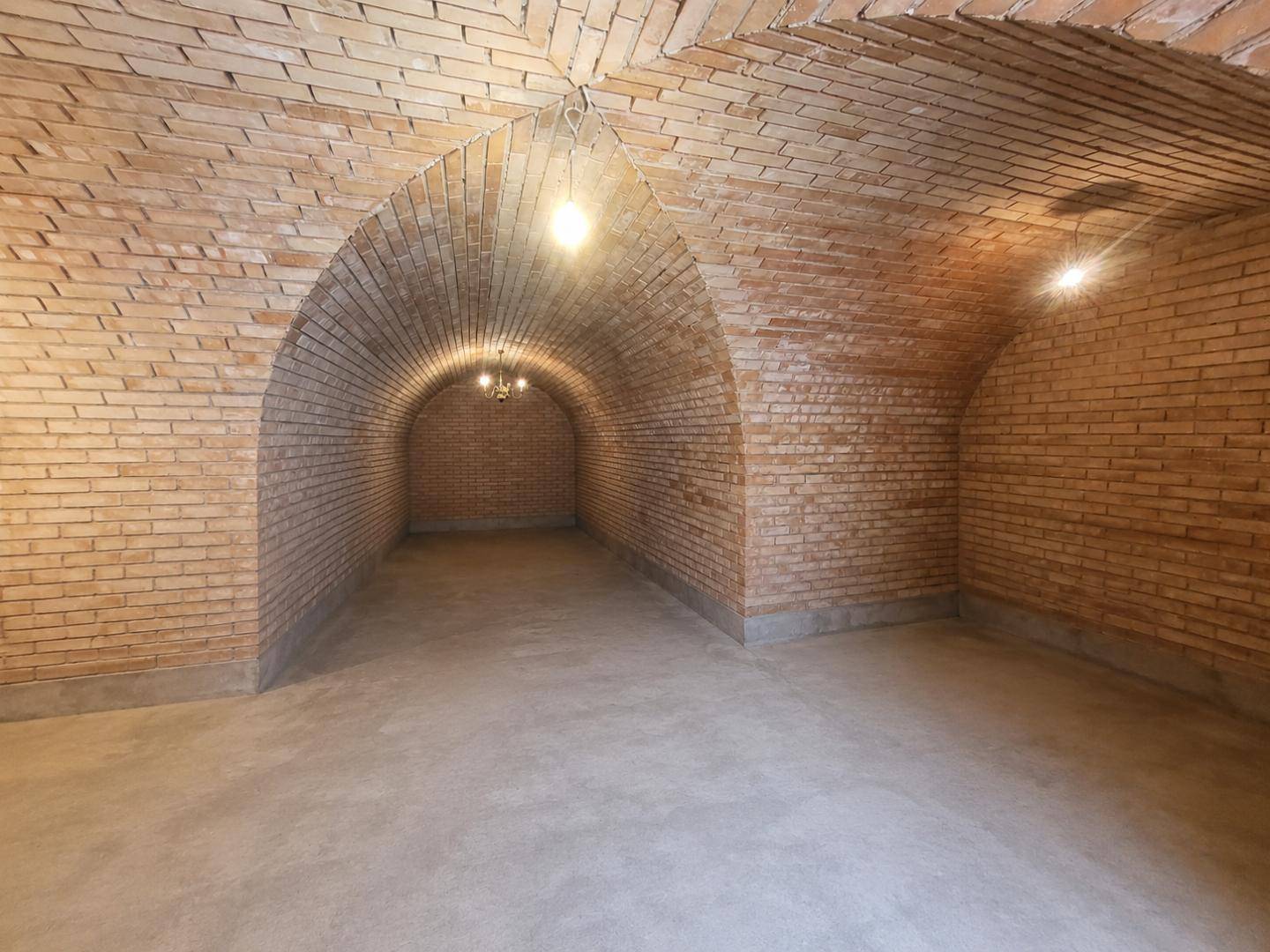 Historischer Gewölbekeller mit unverputzten Ziegelwänden und Betonboden, ideal zur Lagerung.