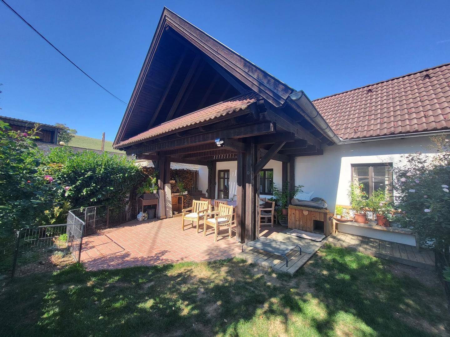Überdachte Terrasse mit Ziegelboden und Holzbalken, ausgestattet mit Gartenmöbeln, ideal für entspannte Stunden im Freien.