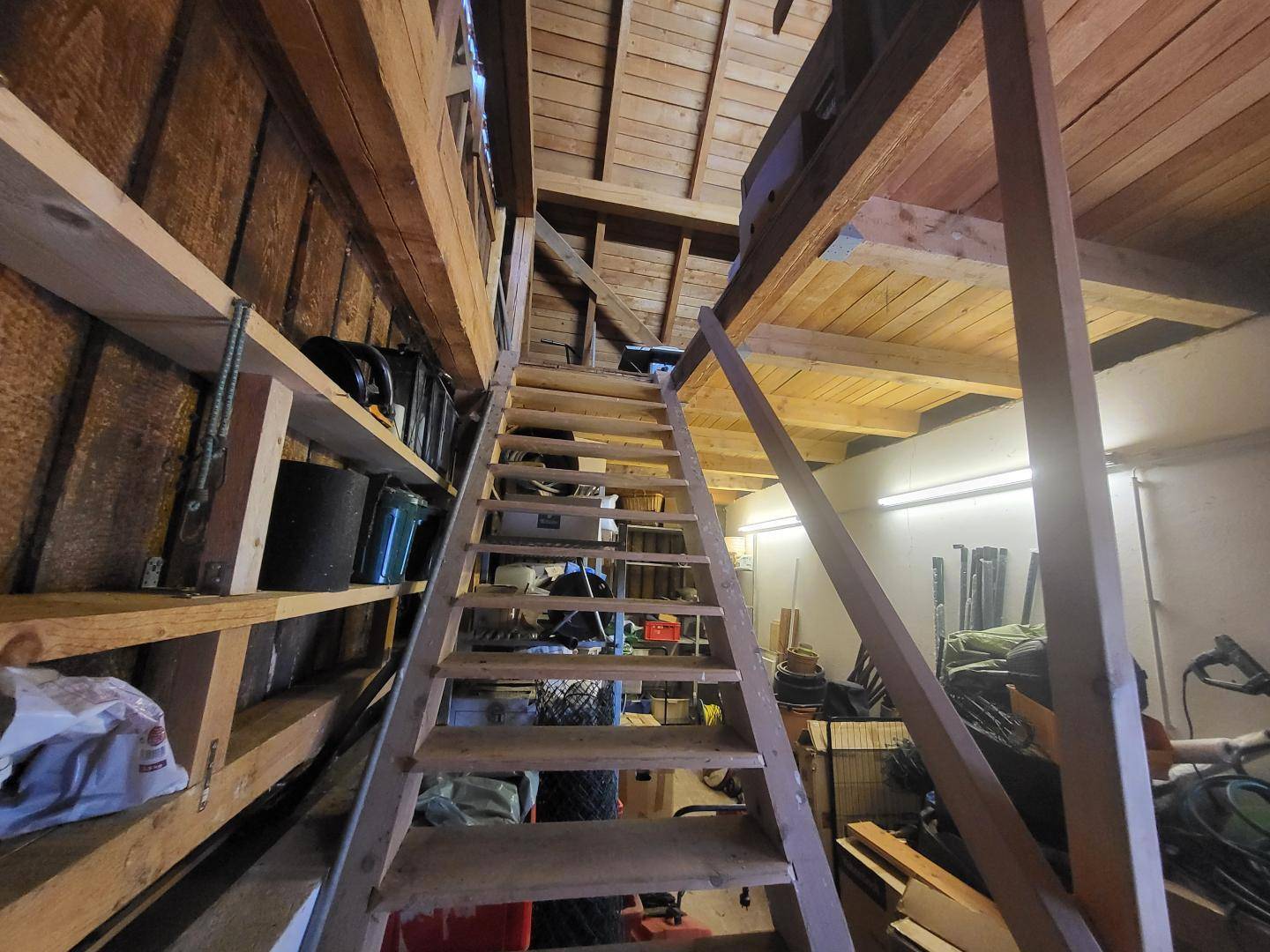 Rustikaler Lagerraum mit Holzkonstruktion, Regalen und einer steilen Holztreppe zum oberen Bereich.