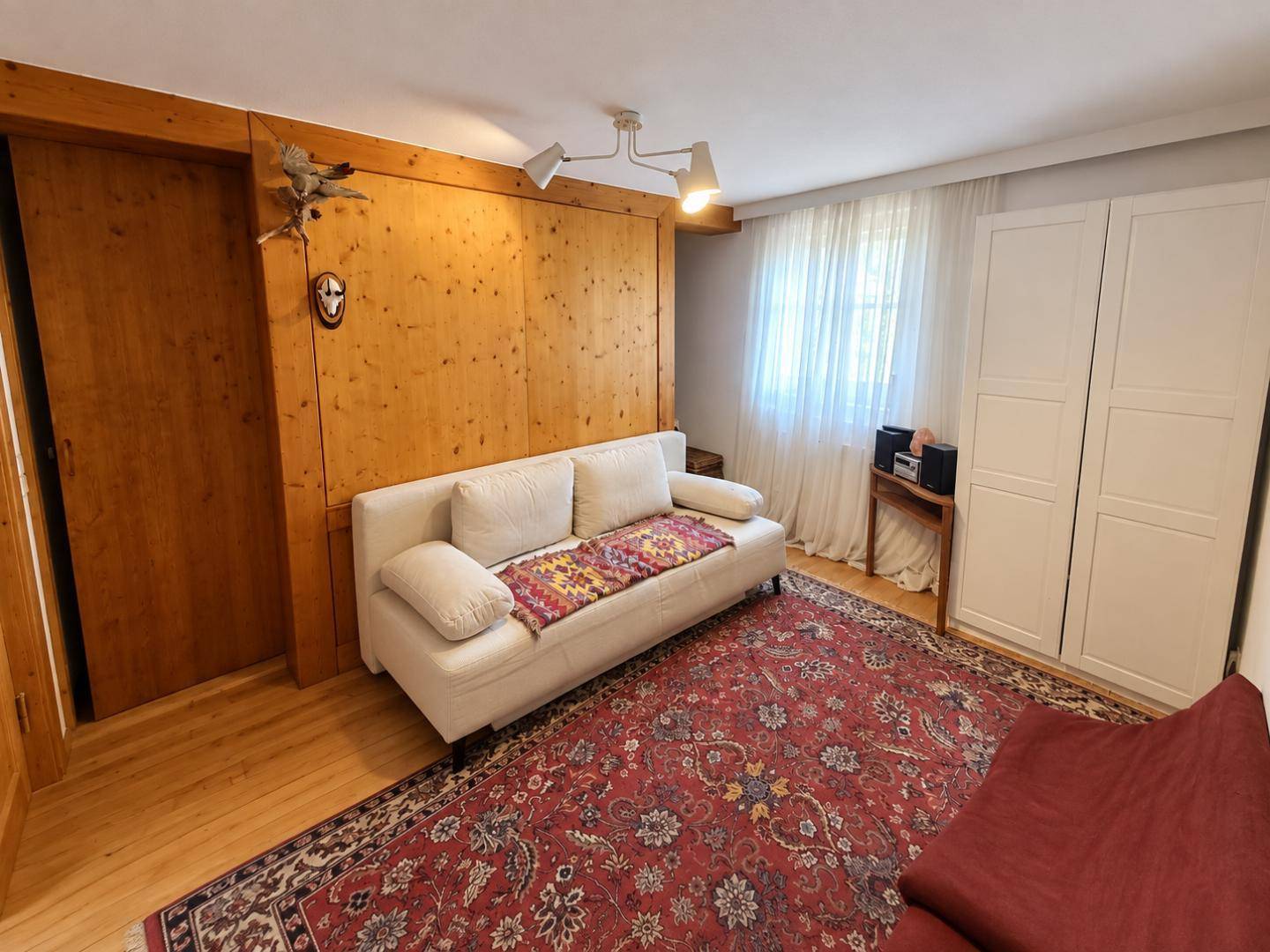 Zimmer mit Holzwandverkleidung, Sofa und Teppich, bietet eine gemütliche Atmosphäre mit viel Tageslicht.