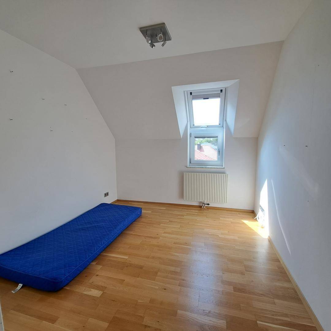 Helles Schlafzimmer mit Holzboden, einem Dachfenster und einer blauen Matratze auf dem Boden.
