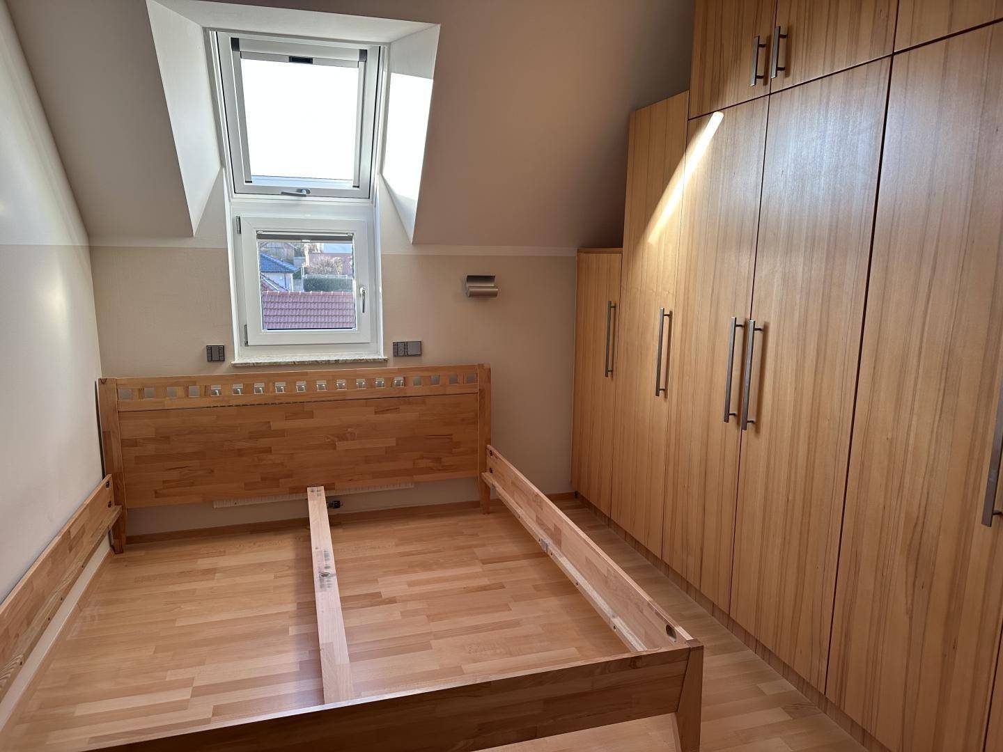 Schlafzimmer mit Holzbettrahmen, Einbauschränken und einem Dachfenster, das viel Licht hereinlässt.
