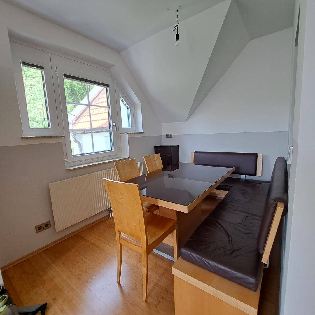 Heller Essbereich mit Holztisch, Stühlen und einer eingebauten Sitzbank unter einer Dachschräge.
