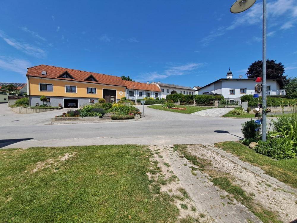 Ländliche Wohngegend mit Häusern, Gärten und einer Straße unter strahlend blauem Himmel.