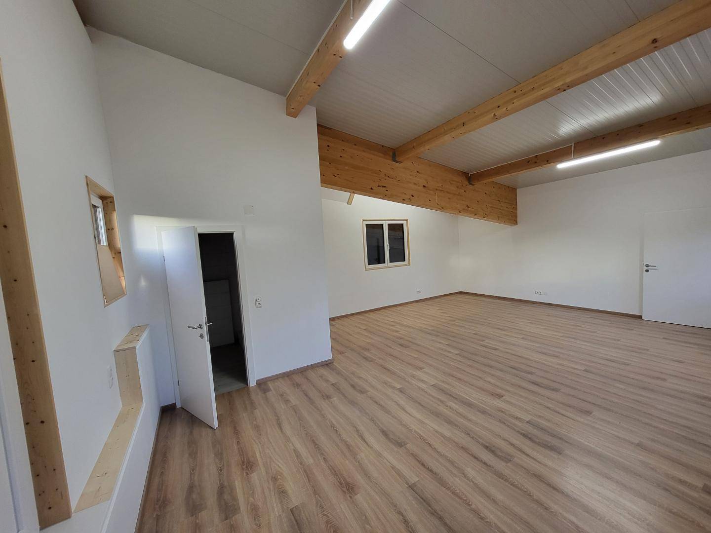 Heller Innenraum mit sichtbaren Holzbalken und neuem Laminatboden, bereit zur Einrichtung.