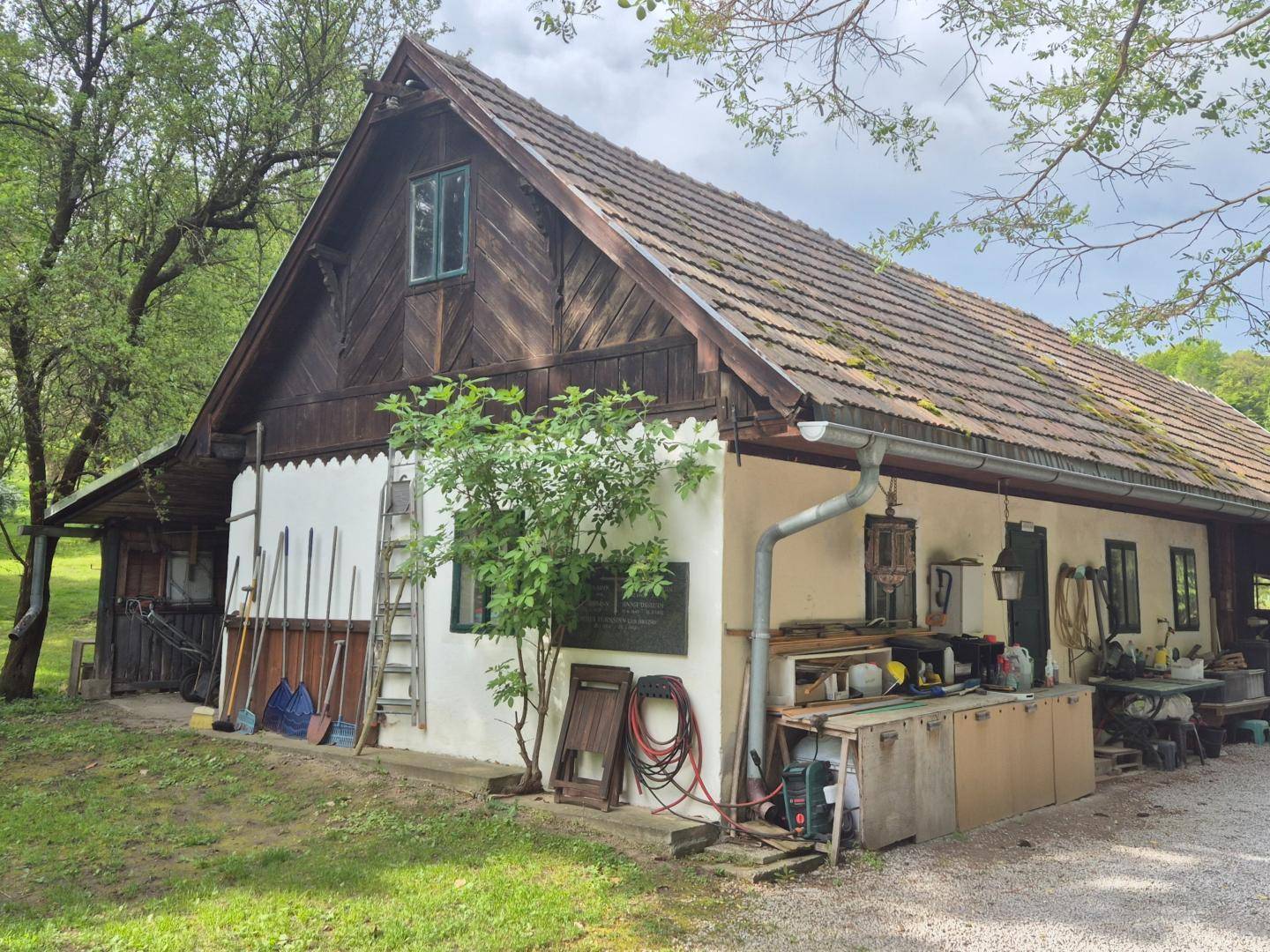 Rustikales altes Bauernhaus mit Holzelementen, Ziegeldach und Arbeitsbereich im Freien.