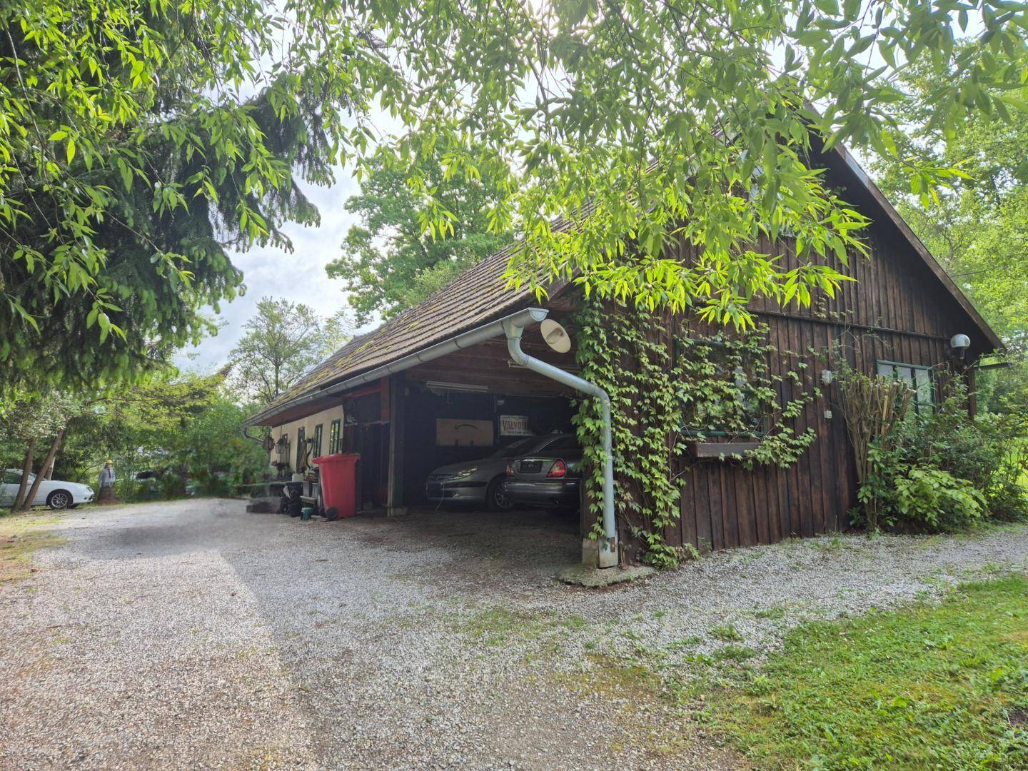 Hölzernes Nebengebäude mit integriertem Carport und bewachsenen Fassaden.