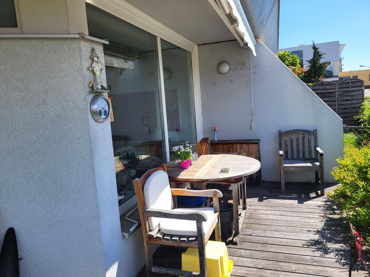 Holzterrasse mit Gartenmöbeln und Zugang zu großen Glasschiebetüren des Gebäudes.