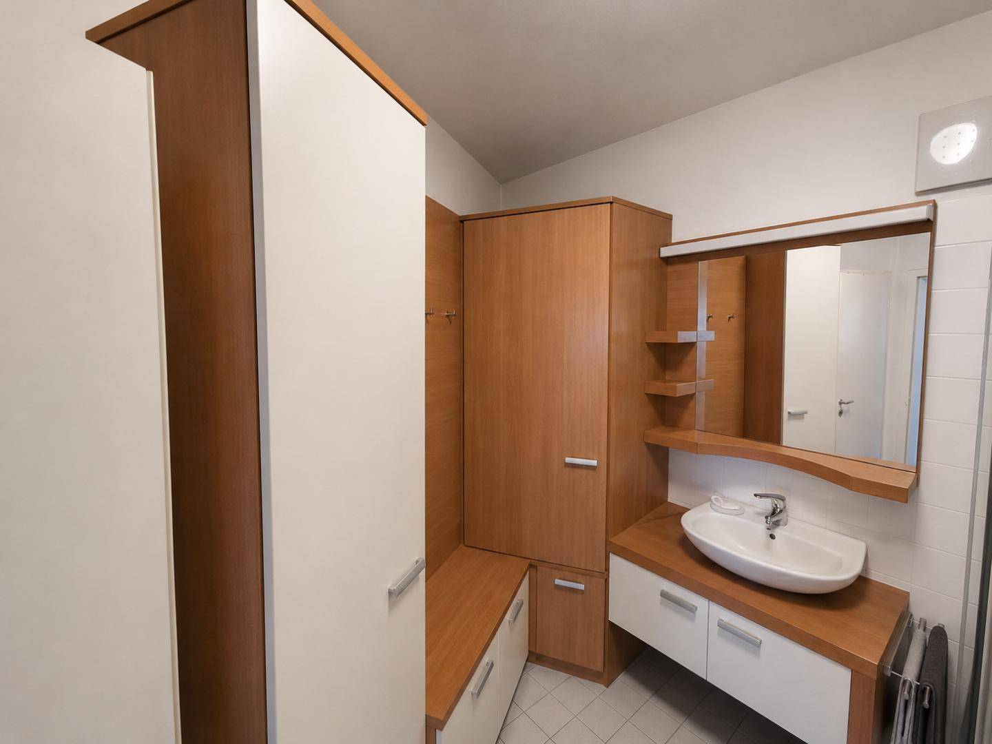 Modernes Badezimmer mit Holzmöbeln, Waschbecken und Spiegel, ausgestattet mit Fliesenboden.