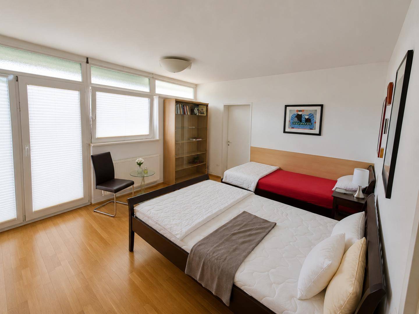 Helles Schlafzimmer mit zwei Betten, Holzfußboden und großen Fenstern mit Jalousien.