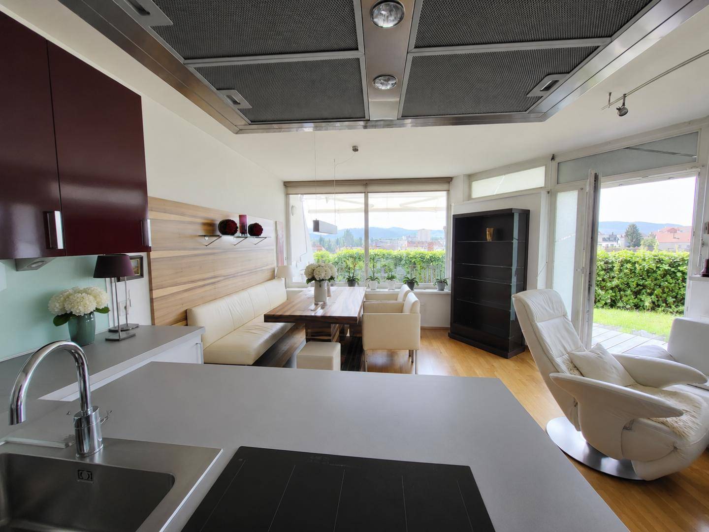 Moderne Küche mit Kochinsel und Essbereich, offen zum hellen Wohnzimmer mit Ausblick.