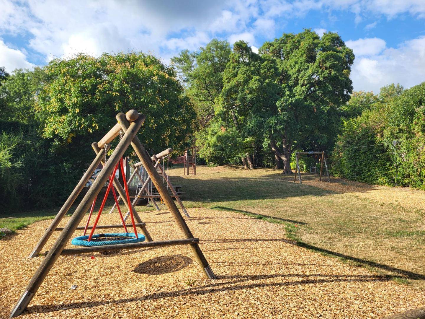 Kinderspielplatz mit Holzschaukeln und Hackschnitzelboden, umgeben von Bäumen und Natur.