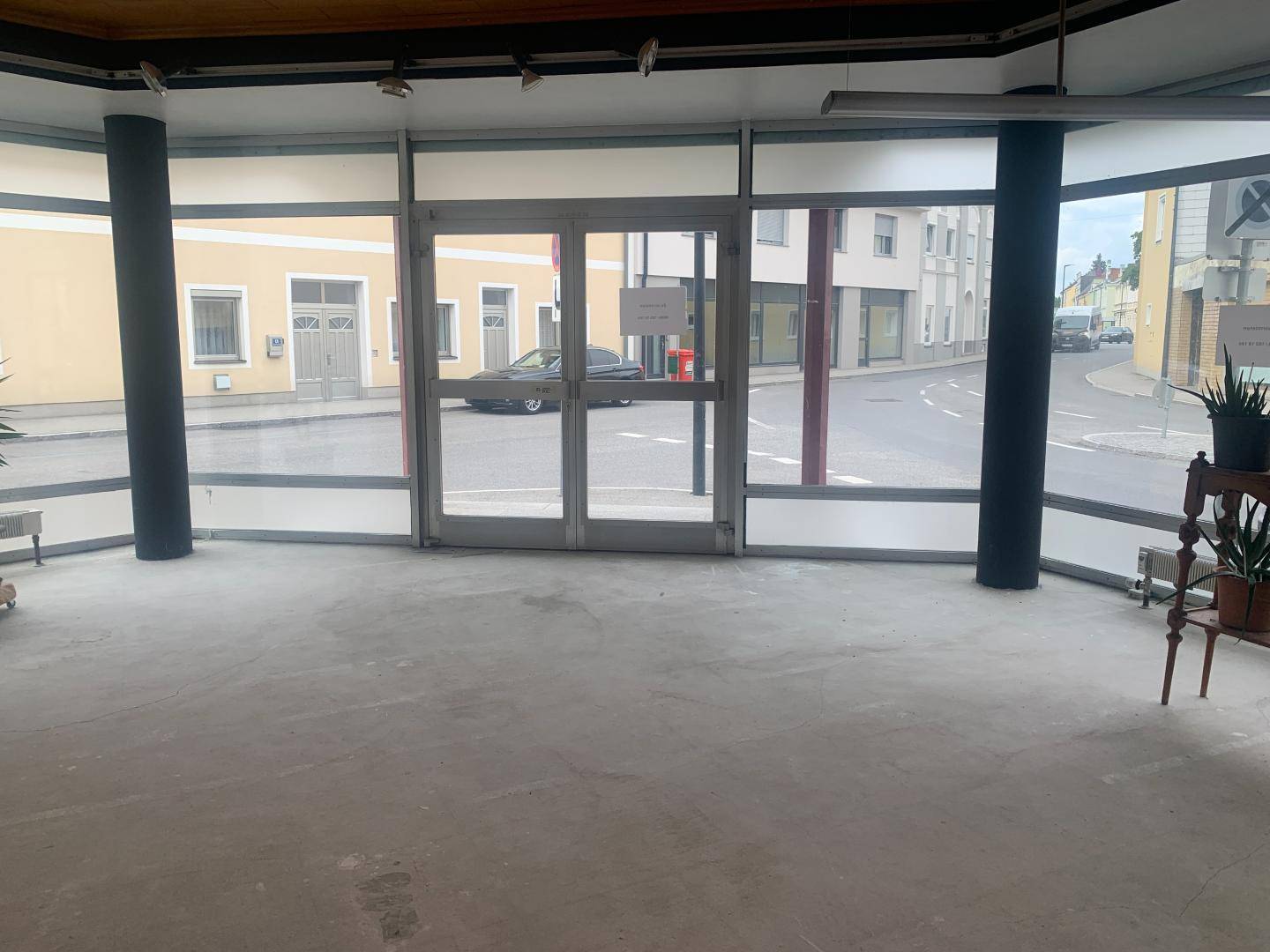 Leerer Ladenraum mit großen Schaufenstern zur Straße, Betonboden und einfacher Beleuchtung.