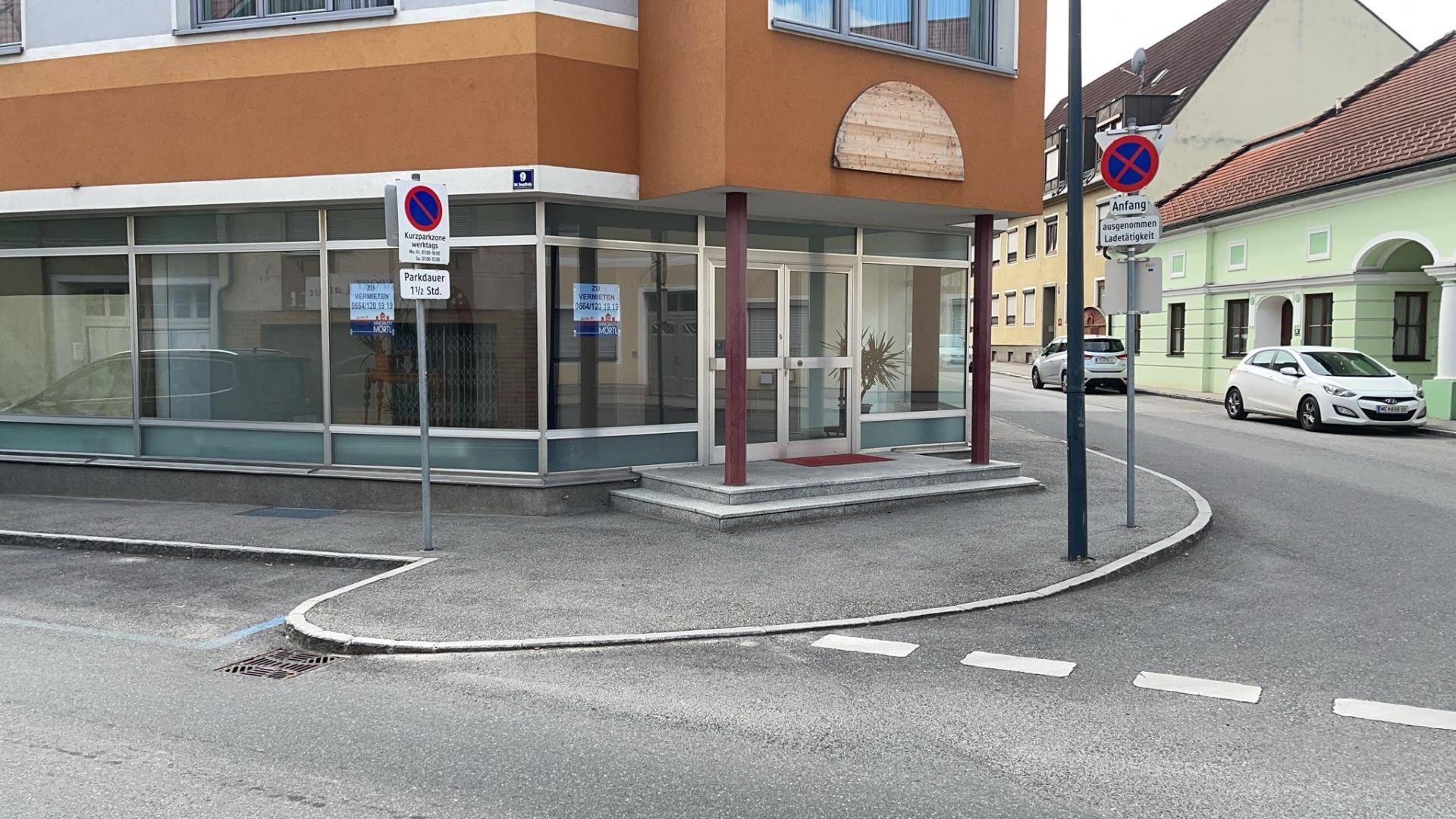 Eckgebäude mit großen Schaufenstern, Bürgersteig und Parkverbotsschildern an der Straßenecke.