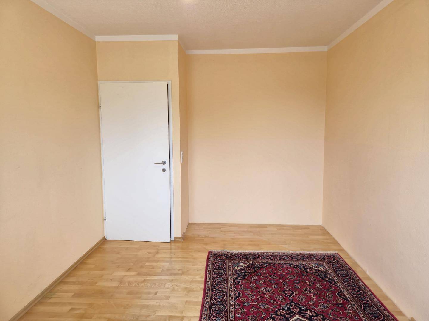 Leeres Zimmer mit Parkettboden und Teppich, bereit zur individuellen Gestaltung.