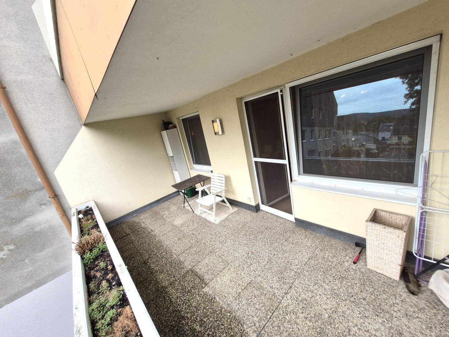 Balkon mit Fliesenboden, kleiner Sitzgelegenheit und Wäscheständer.