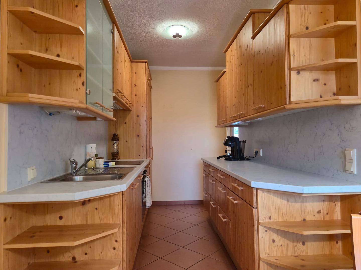 Funktionale Küche mit Holzschränken, hellen Arbeitsplatten und Fliesenboden.