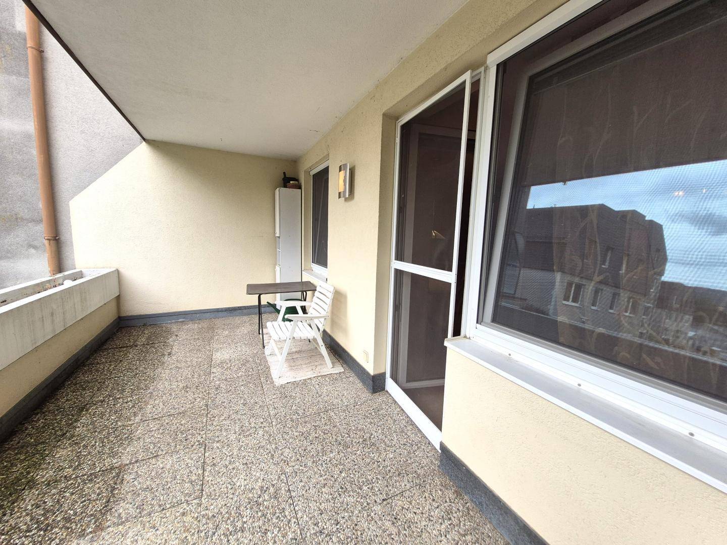 Überdachter Balkon mit Fliesenboden und kleinem Tisch, ideal für entspannte Stunden.