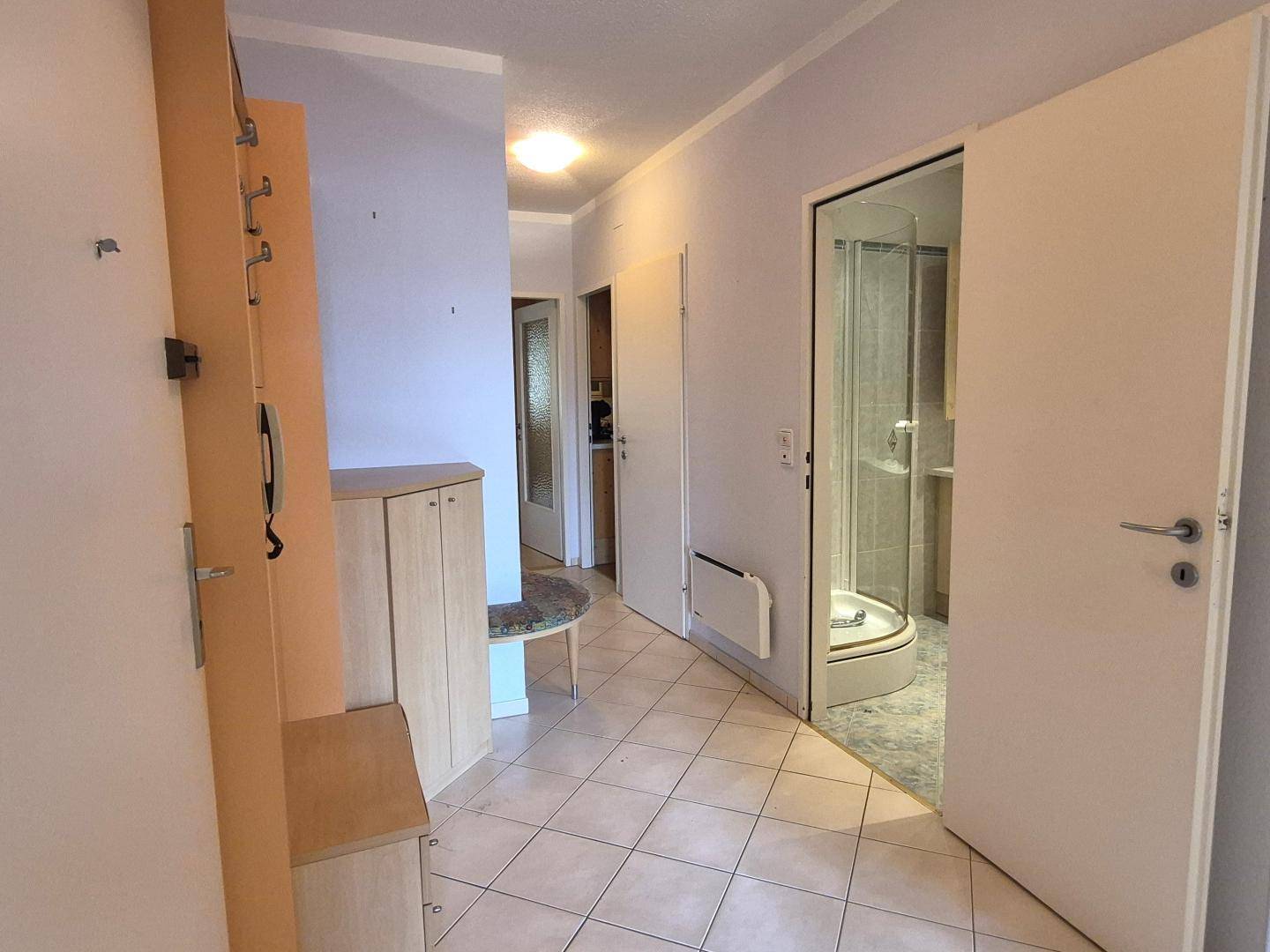 Flur mit Fliesenboden, Garderobe und Blick in das angrenzende Badezimmer.