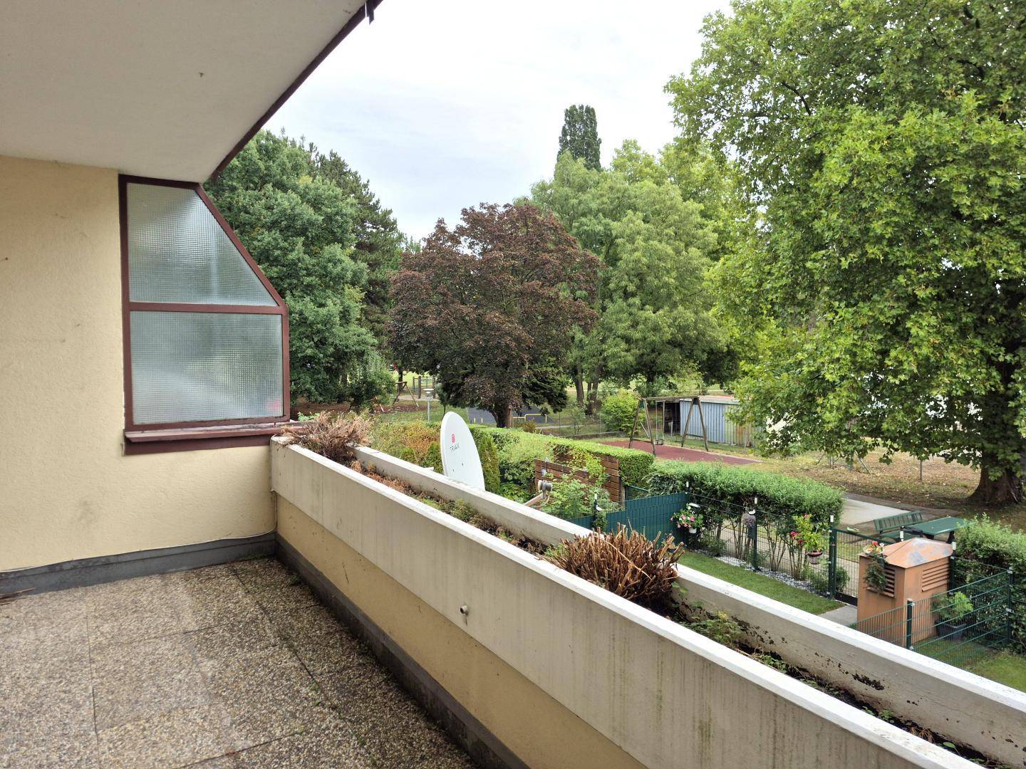 Balkon mit Blick ins Grüne und auf einen Spielplatz, umgeben von Bäumen.
