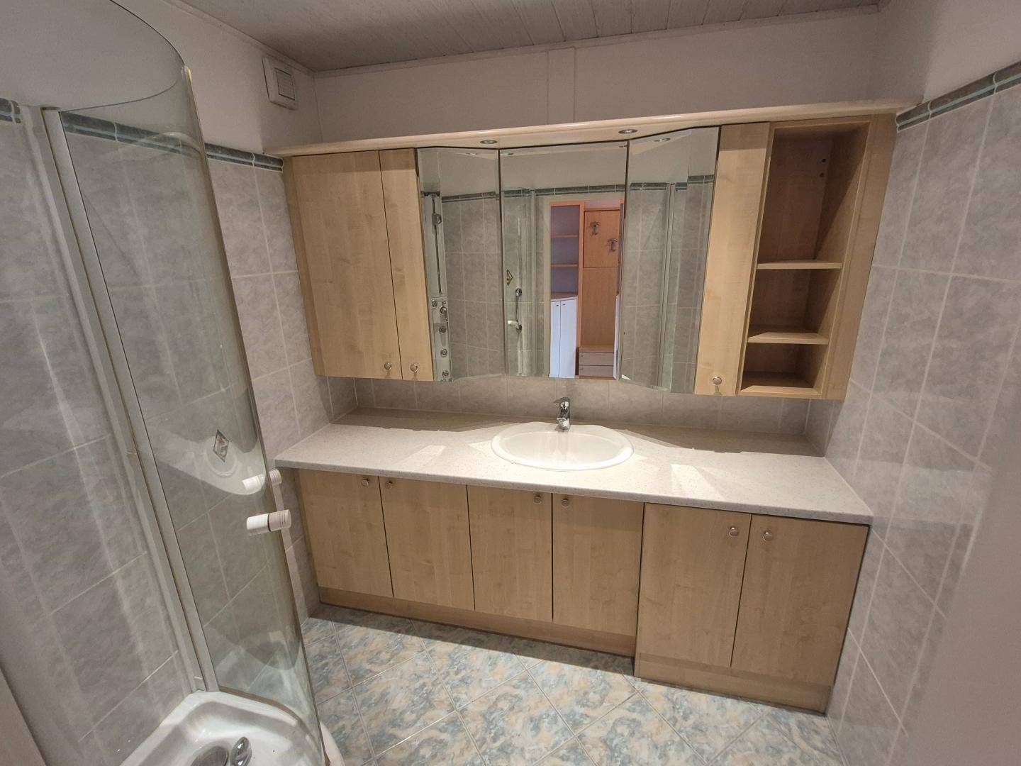 Badezimmer mit Waschtisch, Spiegelschrank und Duschkabine, hell gefliest.