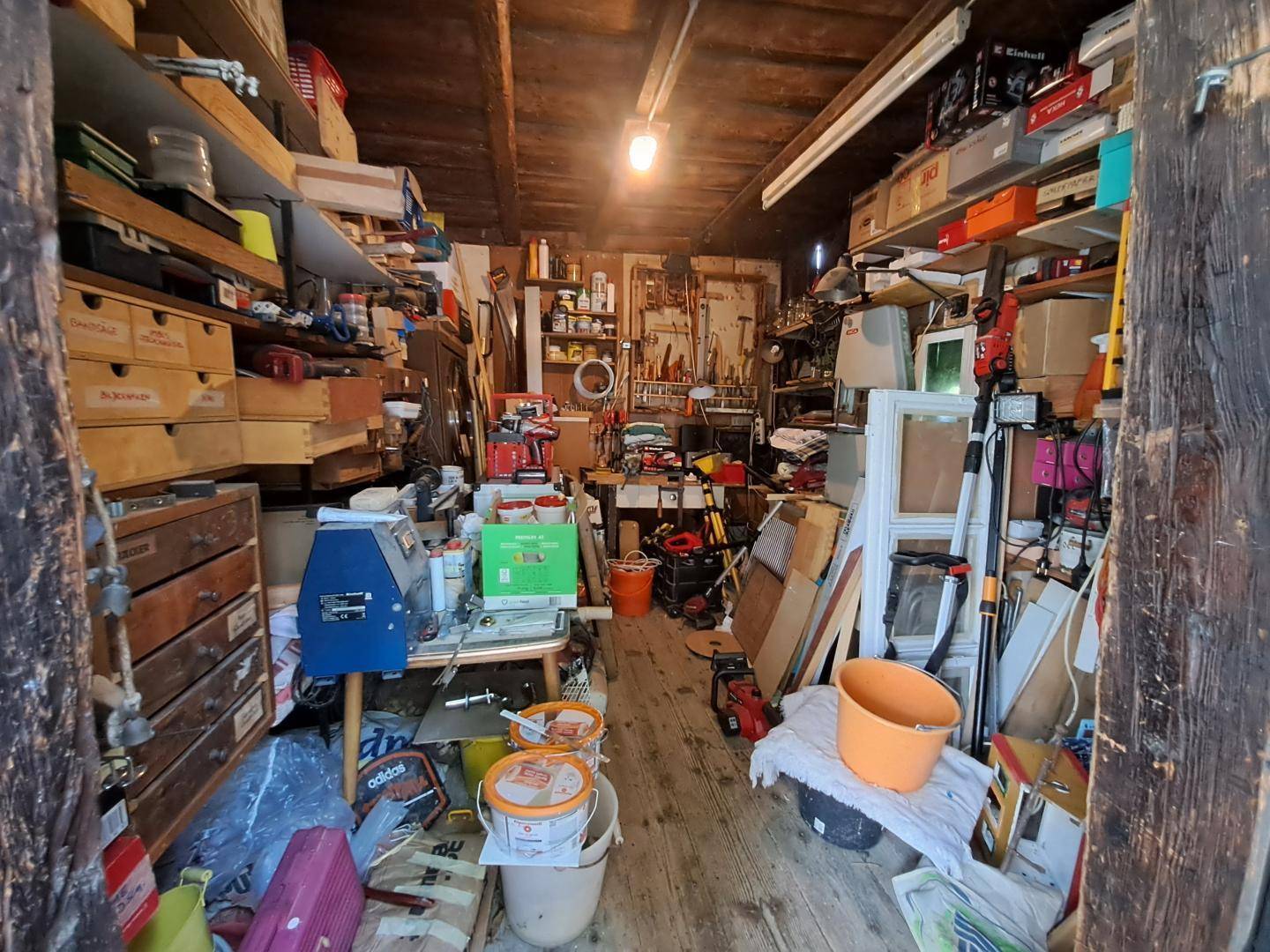 Überfüllter Werkstattraum mit vielen Regalen, Werkzeugen und Materialien.
