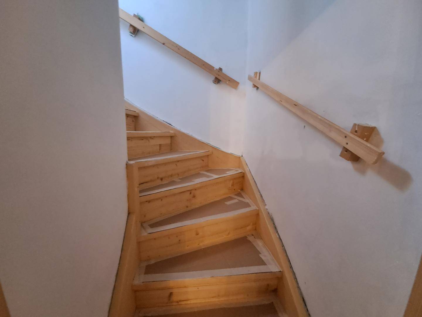 Holztreppe mit einfachen Handläufen, die in das obere Stockwerk führt.