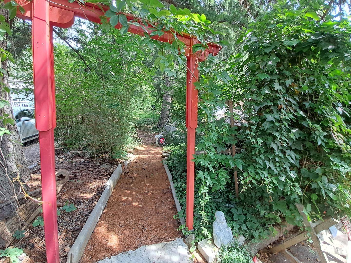 Gartenweg unter einem roten Torbogen, umgeben von üppigem Grün.