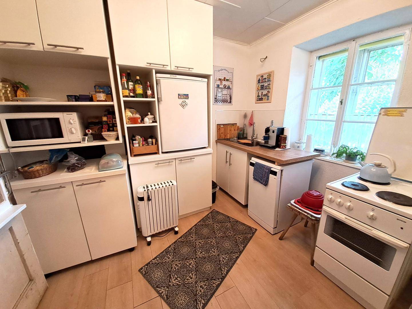 Funktionale Küche mit weißen Schränken, Kühlschrank und kleinem Elektroherd.
