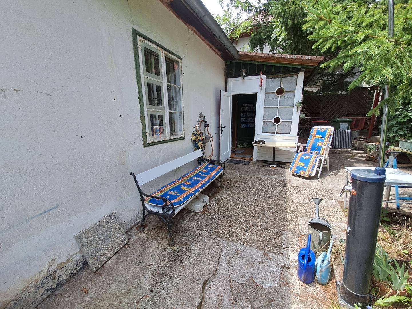Gepflasterter Terrassenbereich am Haus mit Gartenbank und Liegestuhl.
