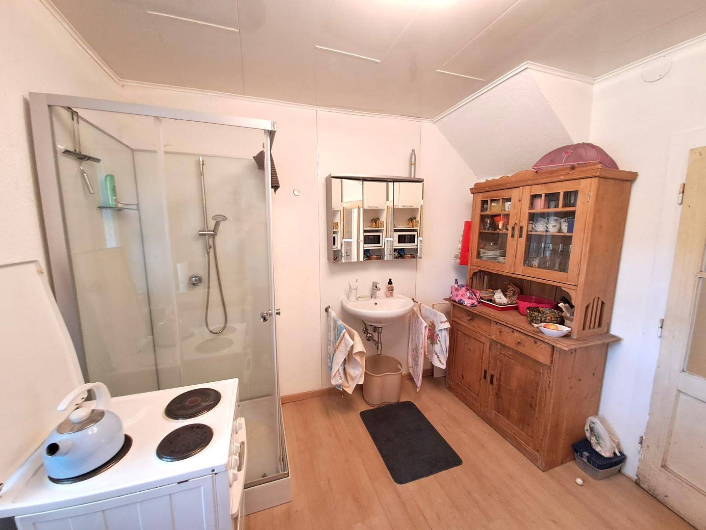 Badezimmer mit Duschkabine, Waschbecken und einem traditionellen Holzschrank.