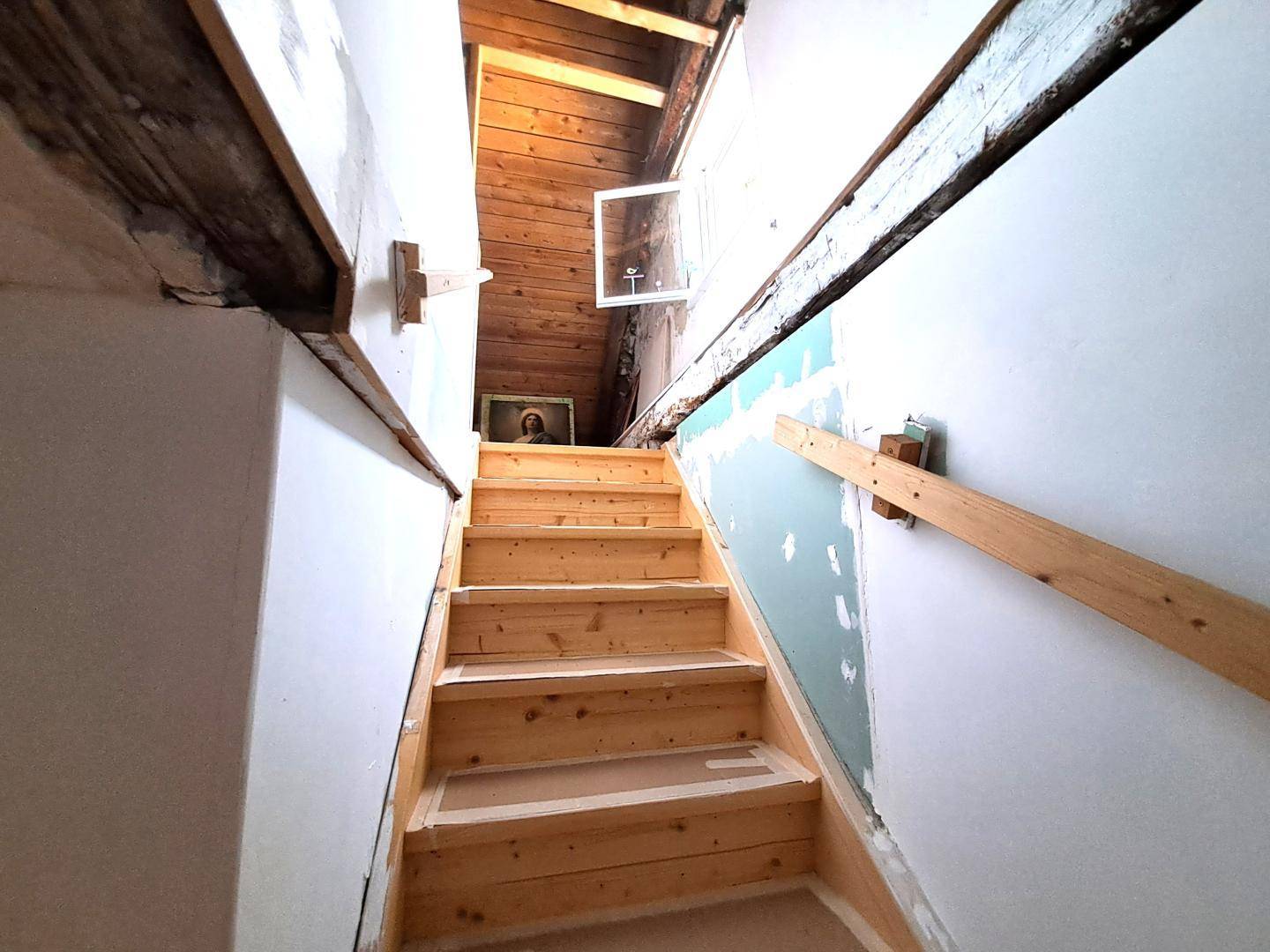 Holztreppe führt zum Dachboden mit sichtbaren Holzbalken und Dachfenster.