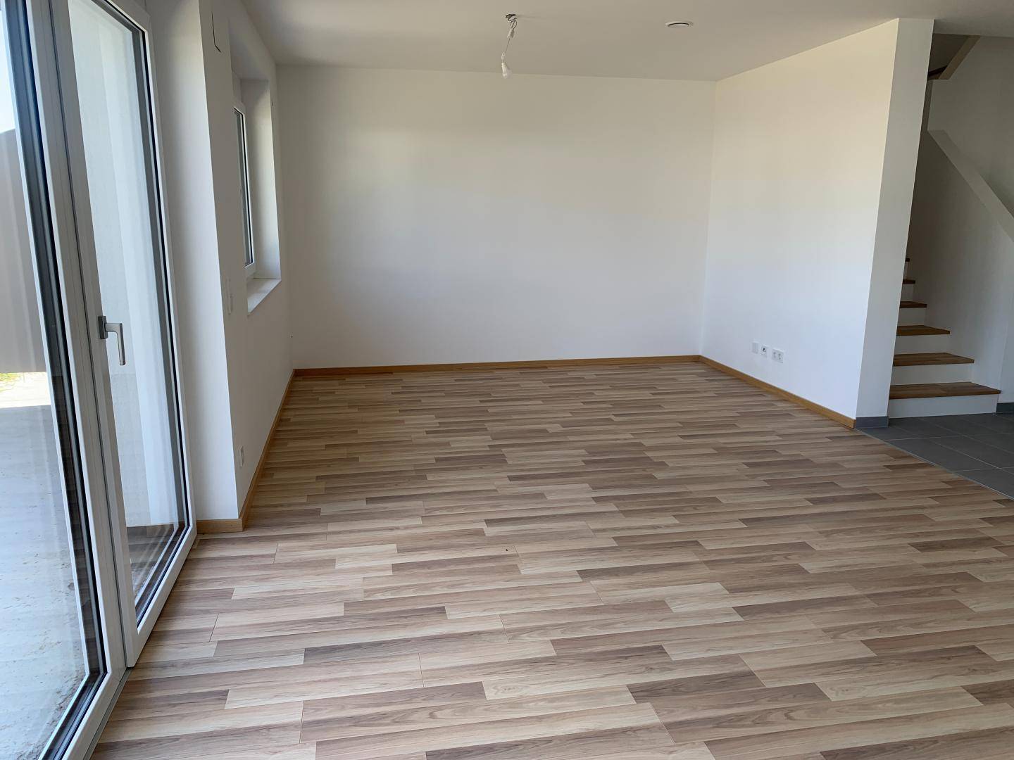 Heller Wohnbereich mit Laminatboden und Zugang zur Terrasse durch eine große Schiebetür.
