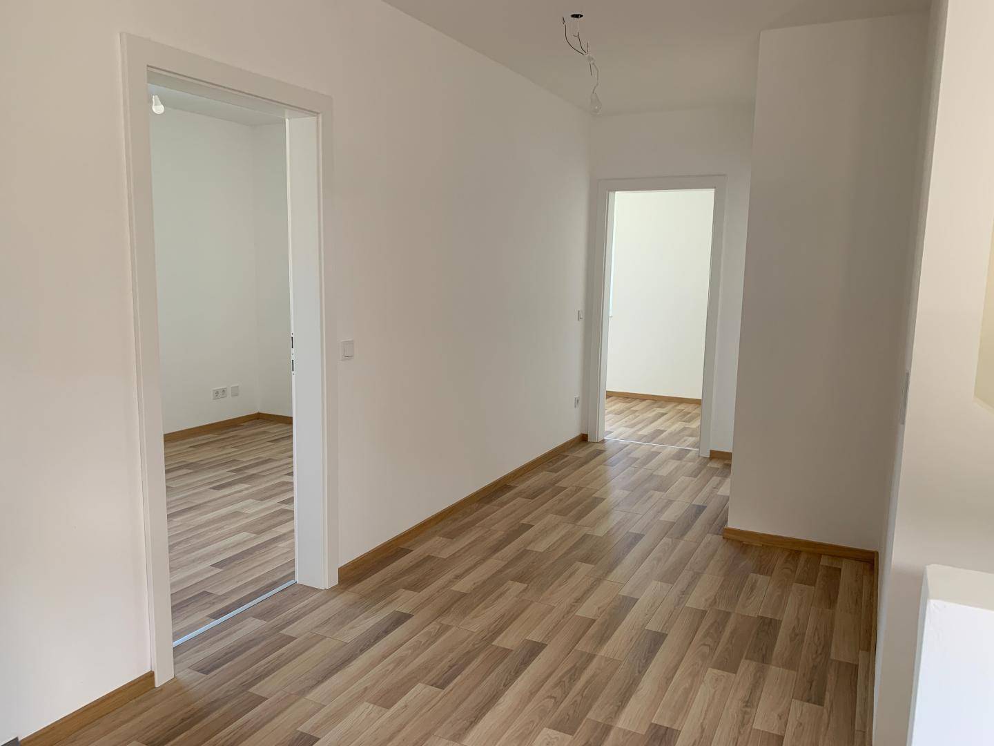 Geräumiger, heller Flur mit Laminatboden und weißen Wänden, der zu weiteren Zimmern führt.