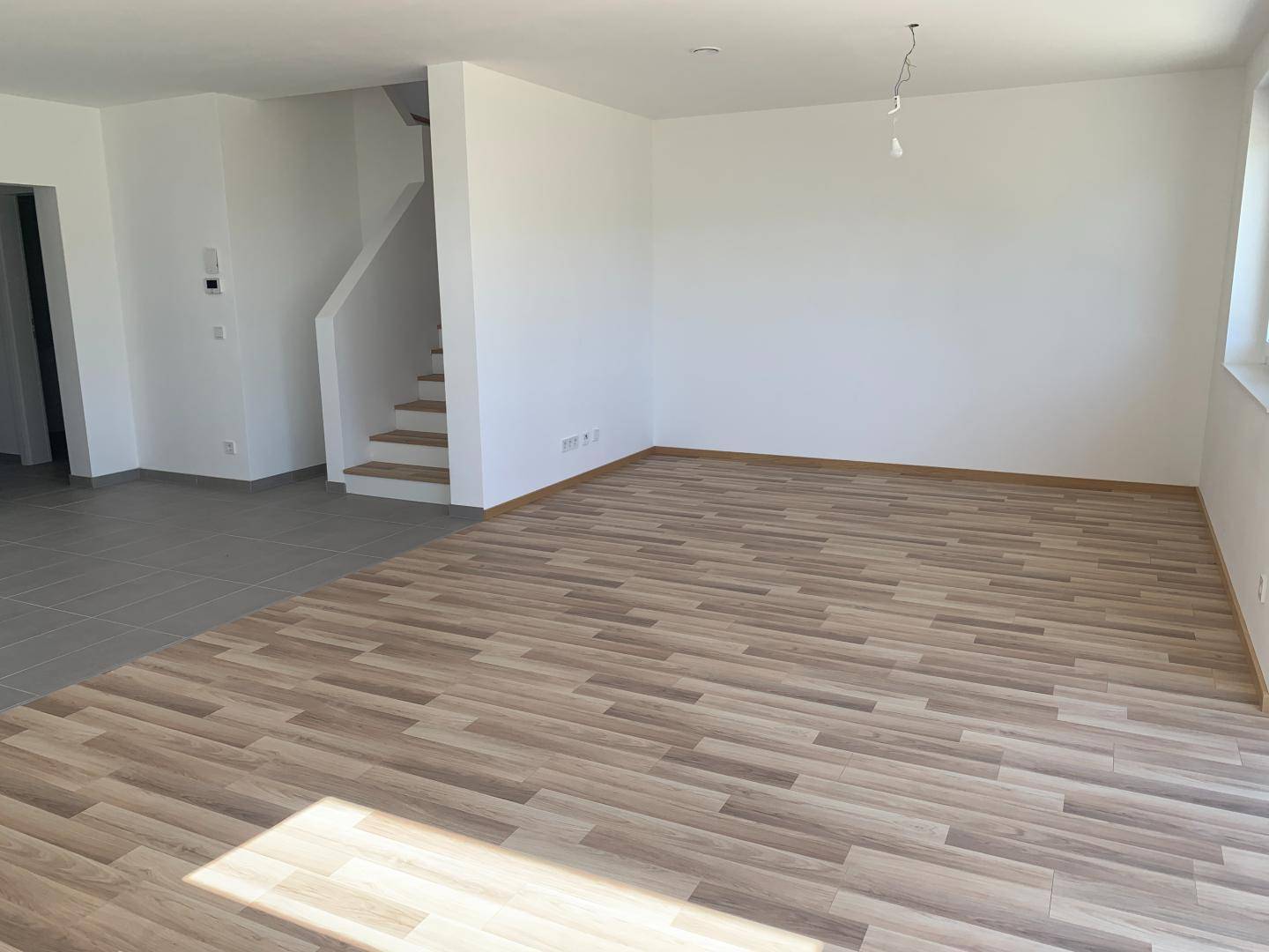 Geräumiger Wohnbereich mit Laminatboden und Treppe zum Obergeschoss, hell und einladend.