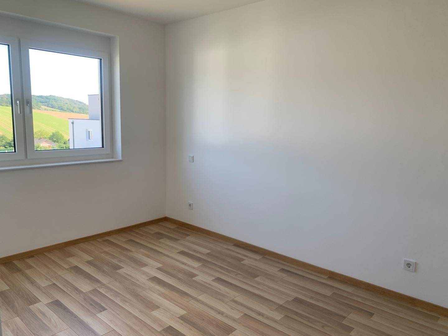 Helles, leeres Zimmer mit Laminatboden und weitem Blick auf die umliegende Landschaft.