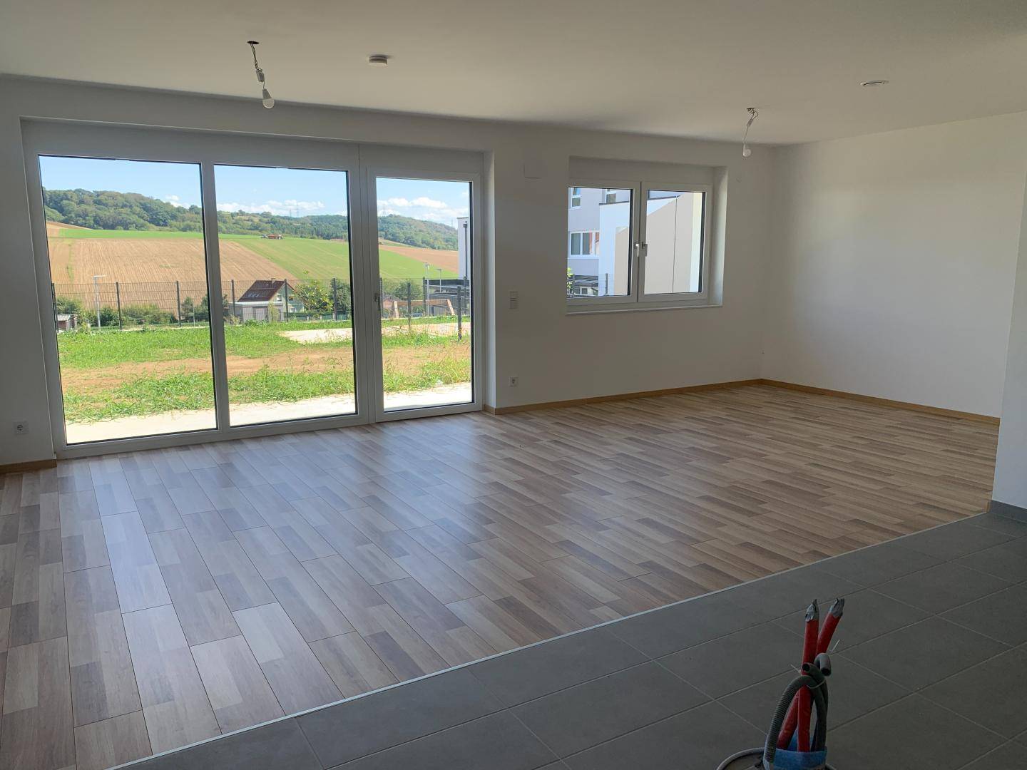 Lichtdurchfluteter Wohnbereich mit großen Fenstern und Schiebetür zum Garten, mit weitem Blick.