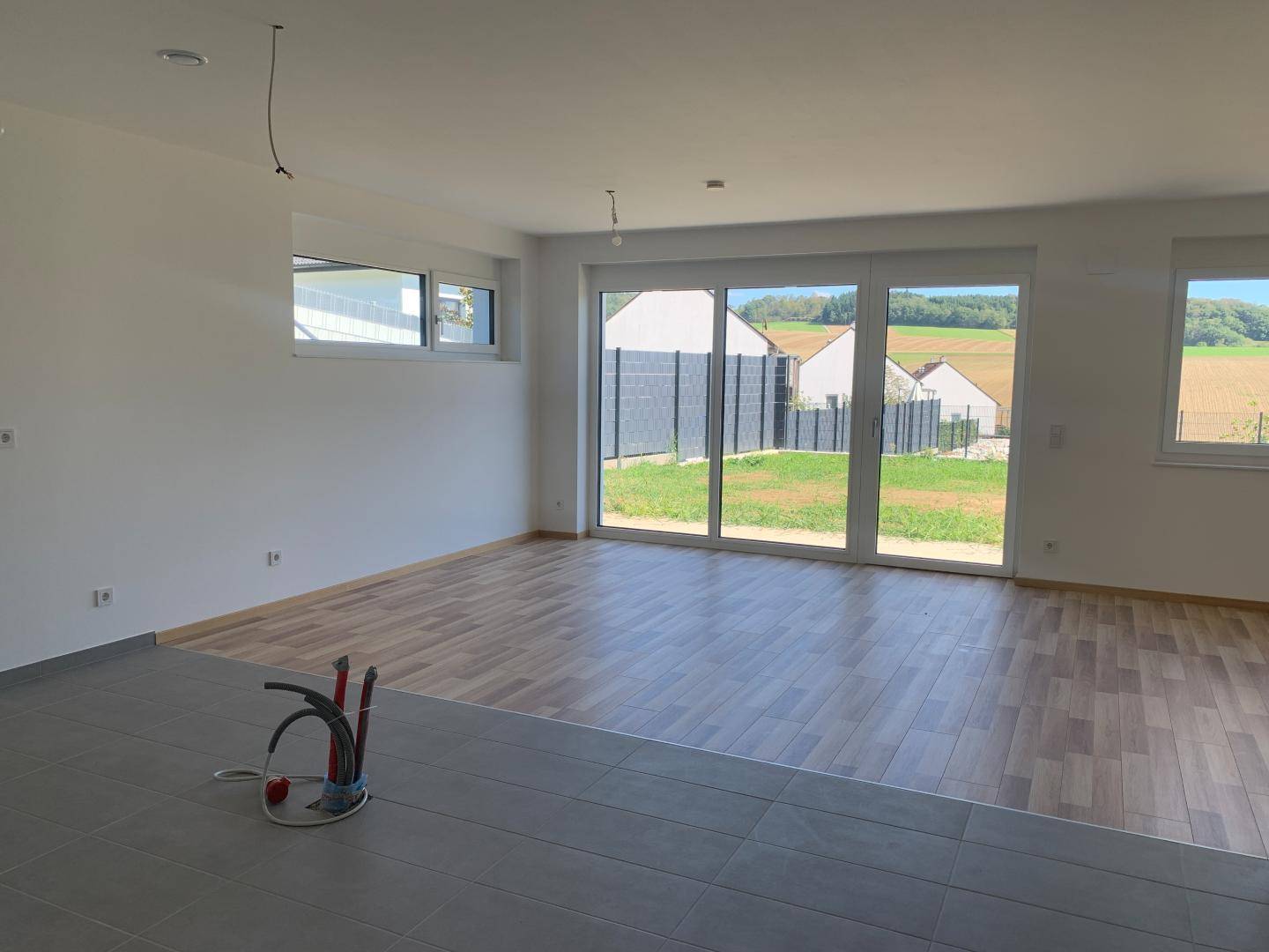 Heller Wohnbereich mit großen Fenstern und Schiebetür zum Garten, mit Blick ins Grüne.
